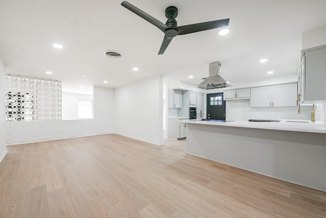 unfurnished living room featuring ceiling fan, light hardwood / wood-style floors, sink, and brick wall