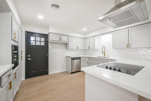 kitchen with appliances with stainless steel finishes, light wood-type flooring, tasteful backsplash, light stone counters, and exhaust hood