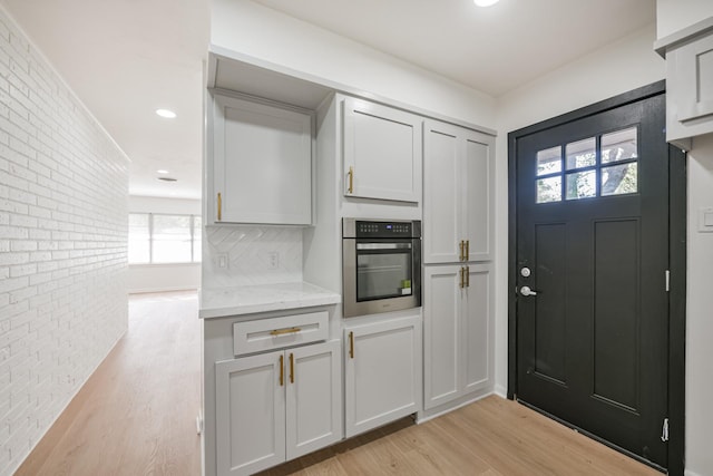 kitchen featuring light stone countertops, light hardwood / wood-style floors, oven, and brick wall