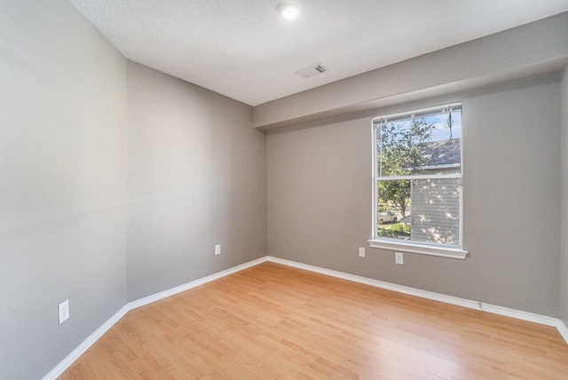 empty room featuring light wood-style flooring, baseboards, visible vents, and a textured ceiling