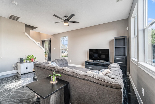 living area with visible vents, a textured ceiling, baseboards, and a ceiling fan