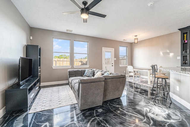 living area featuring plenty of natural light, a textured ceiling, marble finish floor, and a ceiling fan