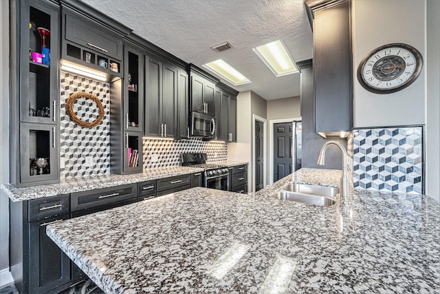 kitchen with dark cabinetry, a peninsula, a sink, stainless steel appliances, and backsplash