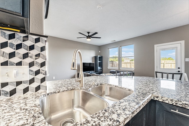 kitchen with light stone counters, sink, ceiling fan, and a textured ceiling