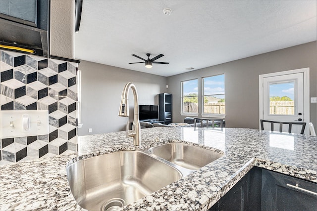 kitchen with ceiling fan, light stone counters, open floor plan, and a sink