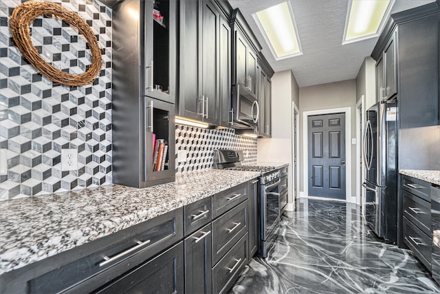 kitchen featuring marble finish floor, light stone counters, a textured ceiling, appliances with stainless steel finishes, and decorative backsplash