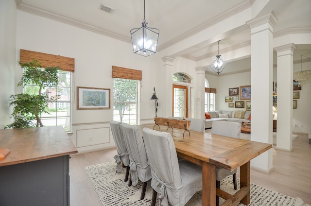 dining space with light hardwood / wood-style floors, an inviting chandelier, decorative columns, and crown molding