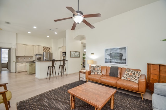 living room with ceiling fan, light wood-type flooring, and a high ceiling