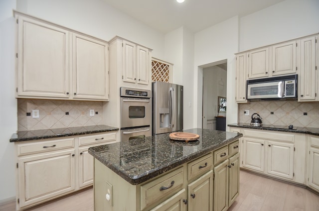 kitchen featuring appliances with stainless steel finishes, backsplash, light hardwood / wood-style flooring, dark stone countertops, and a center island