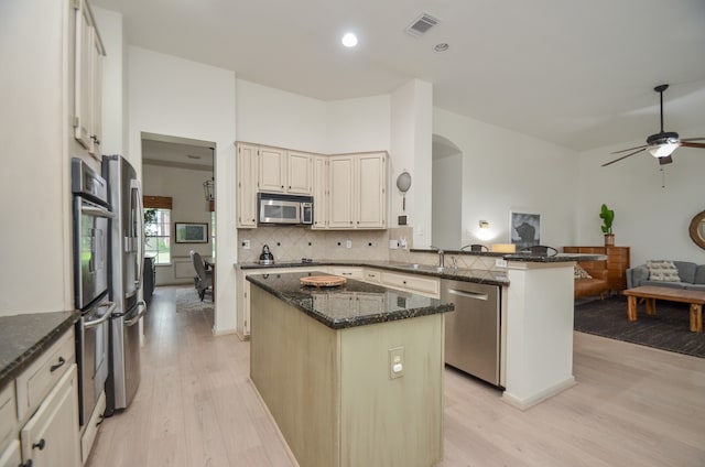 kitchen featuring a center island, dark stone countertops, light hardwood / wood-style floors, kitchen peninsula, and stainless steel appliances