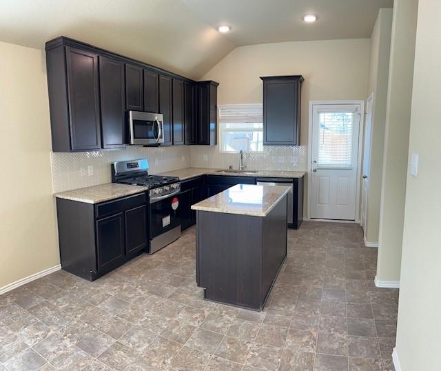 kitchen with appliances with stainless steel finishes, light stone counters, vaulted ceiling, sink, and a kitchen island