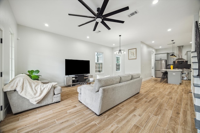 living room with light hardwood / wood-style floors and ceiling fan with notable chandelier