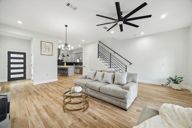 living room with ceiling fan with notable chandelier and light hardwood / wood-style floors