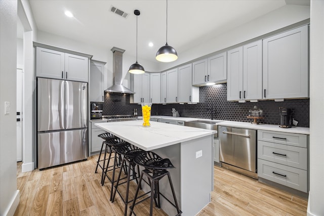 kitchen featuring decorative backsplash, stainless steel appliances, wall chimney range hood, and light wood-type flooring