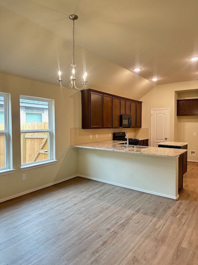 kitchen with an inviting chandelier, vaulted ceiling, light wood-type flooring, light stone counters, and kitchen peninsula