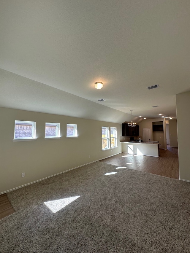 unfurnished living room with hardwood / wood-style floors, lofted ceiling, and a notable chandelier