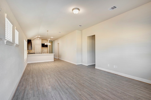 unfurnished living room featuring a chandelier, hardwood / wood-style floors, and vaulted ceiling