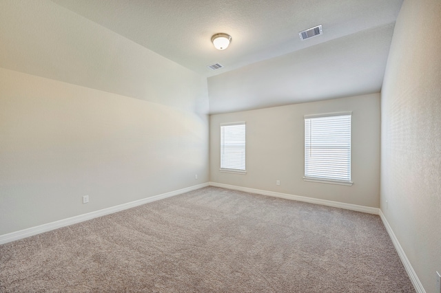 empty room with a textured ceiling, carpet floors, and vaulted ceiling