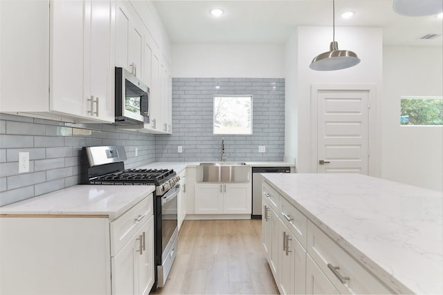 9339 Lavender St, North Houston, TX 77016 - kitchen featuring stainless steel appliances, white cabinets, backsplash, light wood finished floors, and light stone counters