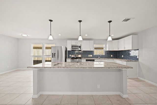 kitchen with appliances with stainless steel finishes, light stone counters, white cabinets, a center island, and hanging light fixtures