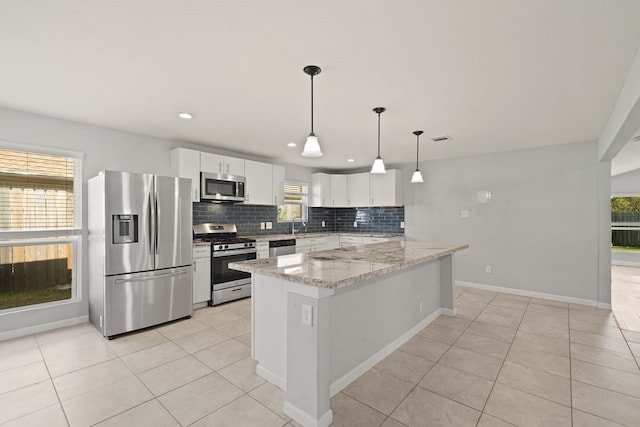 kitchen with light stone countertops, appliances with stainless steel finishes, tasteful backsplash, decorative light fixtures, and white cabinetry