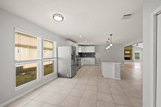 kitchen with hanging light fixtures, white cabinets, backsplash, a kitchen island, and appliances with stainless steel finishes