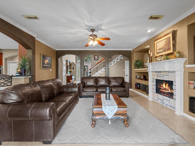 tiled living room featuring a fireplace, built in shelves, ceiling fan, and ornamental molding