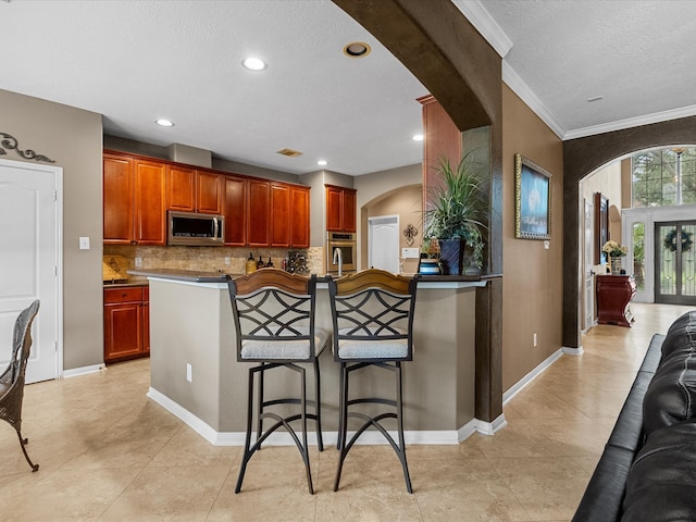 kitchen with a kitchen bar, appliances with stainless steel finishes, tasteful backsplash, ornamental molding, and light tile patterned floors