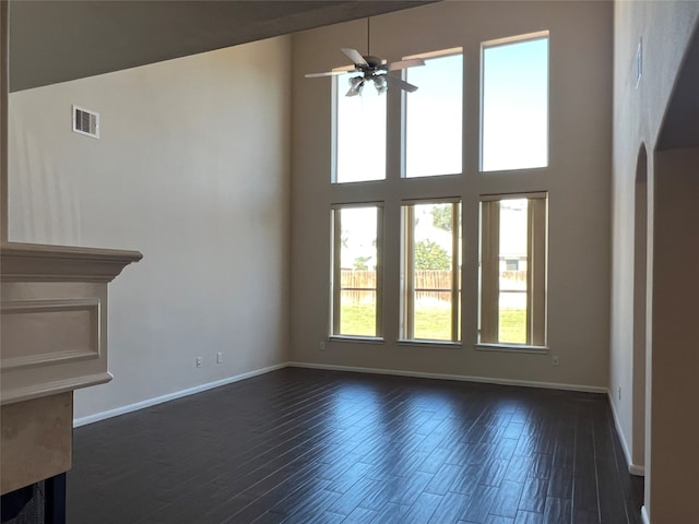 unfurnished living room with a towering ceiling, ceiling fan, and dark wood-type flooring