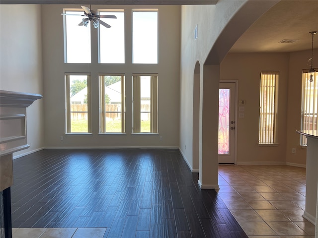 unfurnished living room featuring dark hardwood / wood-style floors, ceiling fan, and a towering ceiling