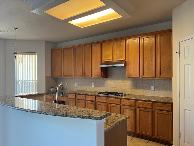 kitchen with a kitchen island with sink, sink, decorative backsplash, decorative light fixtures, and stainless steel gas cooktop