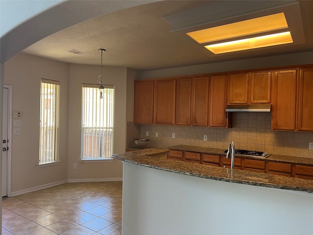 kitchen featuring tasteful backsplash, stainless steel gas cooktop, stone countertops, hanging light fixtures, and light tile patterned flooring