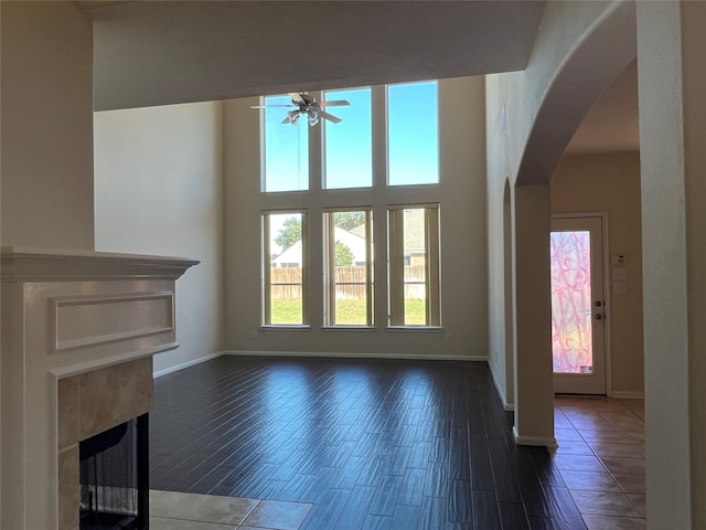 unfurnished living room featuring a high ceiling, dark hardwood / wood-style floors, ceiling fan, and a tiled fireplace