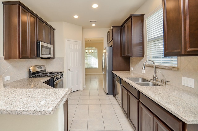 kitchen featuring backsplash, sink, appliances with stainless steel finishes, a notable chandelier, and light stone counters