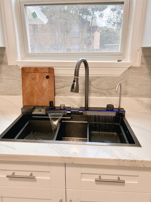 interior details featuring decorative backsplash, light stone countertops, white cabinetry, and sink