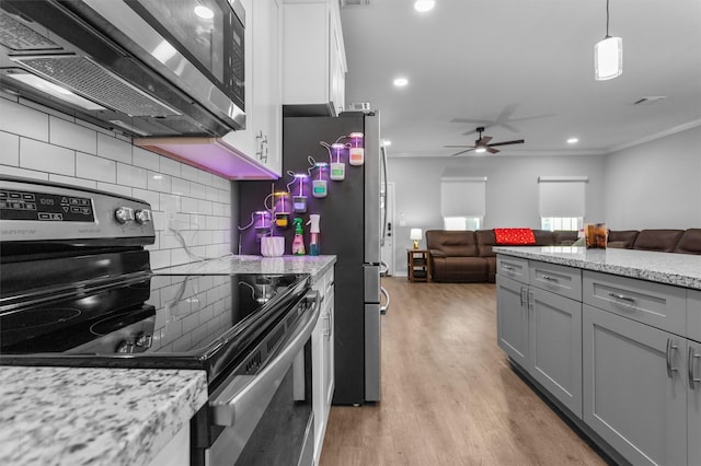 kitchen with backsplash, white cabinets, hanging light fixtures, appliances with stainless steel finishes, and light hardwood / wood-style floors