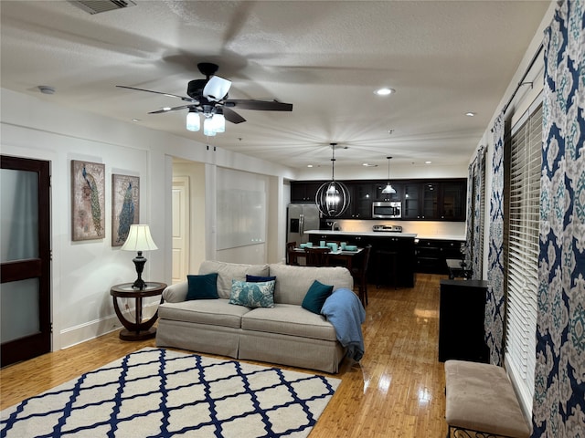 living room featuring ceiling fan, light hardwood / wood-style flooring, and a textured ceiling