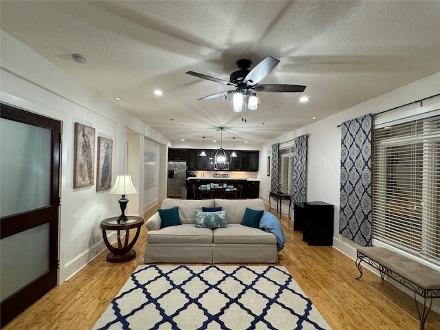 living room featuring ceiling fan, light hardwood / wood-style floors, and a textured ceiling