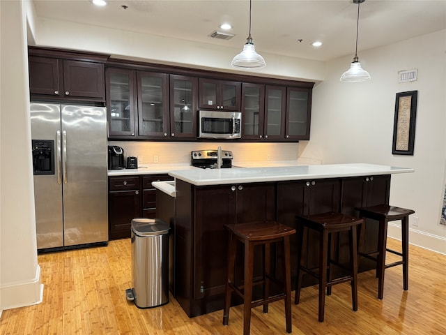 bar with hanging light fixtures, decorative backsplash, light wood-type flooring, dark brown cabinets, and stainless steel appliances