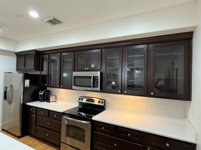 2208 Post Office St Unit 105, Galveston, TX 77550 - kitchen with stainless steel appliances, dark brown cabinets, decorative backsplash, and glass insert cabinets