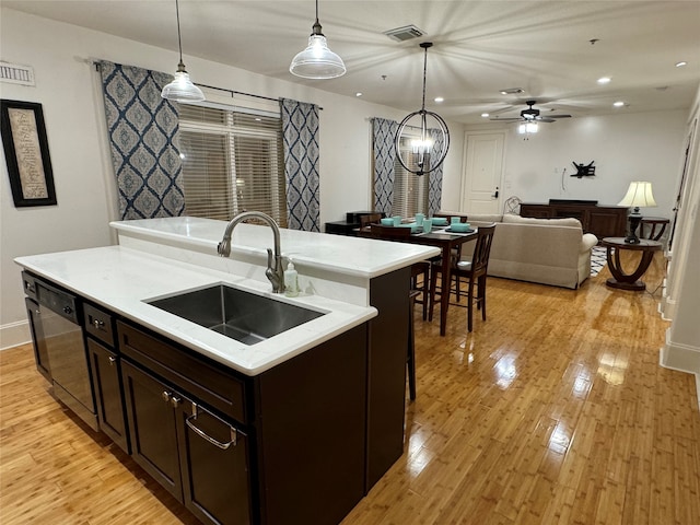 kitchen with dishwasher, sink, light hardwood / wood-style floors, decorative light fixtures, and a center island with sink