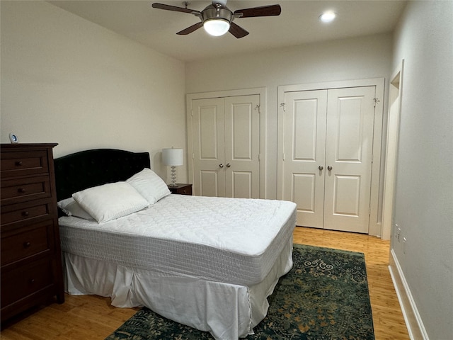 bedroom with light wood-type flooring, ceiling fan, and multiple closets