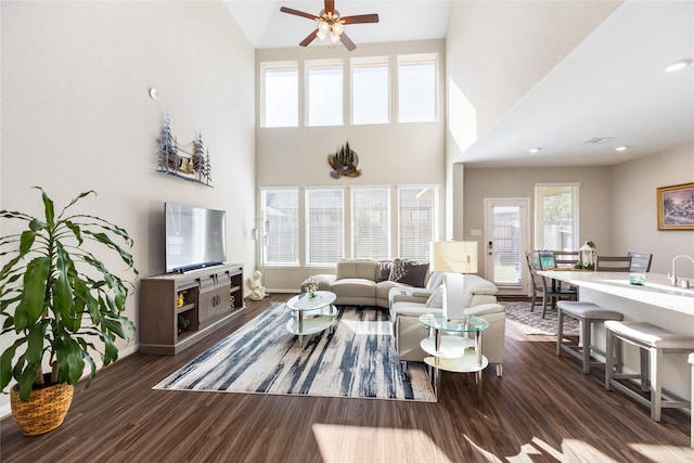 living room with a towering ceiling, dark hardwood / wood-style floors, and ceiling fan