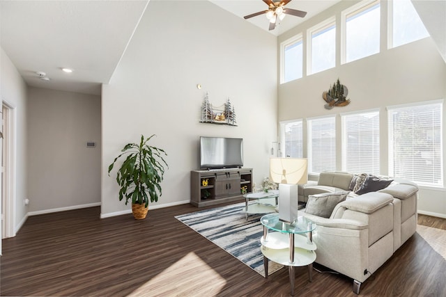 living room with ceiling fan, a towering ceiling, dark wood-type flooring, and a healthy amount of sunlight