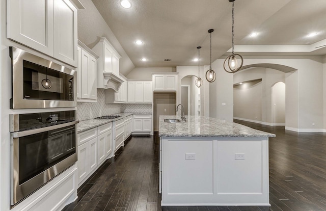 kitchen with pendant lighting, built in microwave, white cabinetry, sink, and a center island with sink