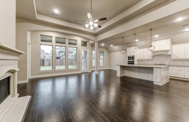 unfurnished living room featuring ceiling fan, dark hardwood / wood-style floors, a fireplace, and a tray ceiling