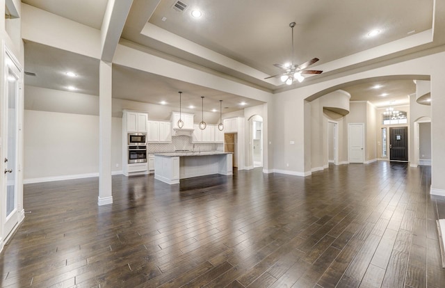 living room featuring a raised ceiling, dark wood-type flooring, and ceiling fan