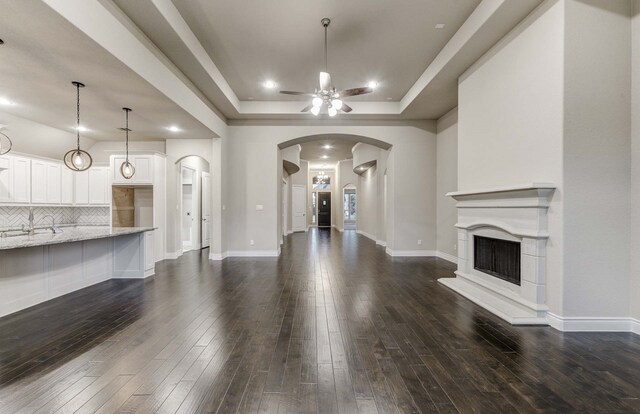 unfurnished living room with ceiling fan, dark hardwood / wood-style flooring, and a tray ceiling