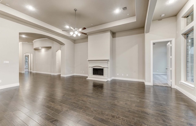 unfurnished living room featuring dark wood-type flooring, a raised ceiling, and ceiling fan