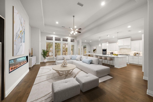 living room featuring ceiling fan, dark hardwood / wood-style flooring, a raised ceiling, and sink